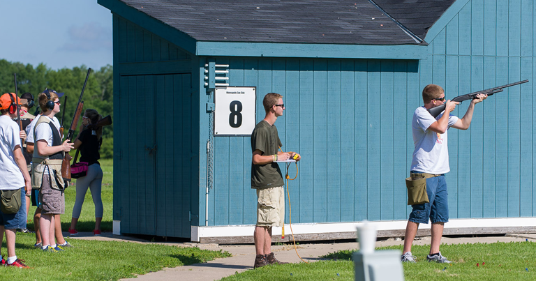 A group of people with riffles standing in front of a blue shed.
